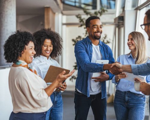 A diverse group of professionals smiling and shaking hands in a modern office environment. The image conveys teamwork, collaboration, and positive business relationships.